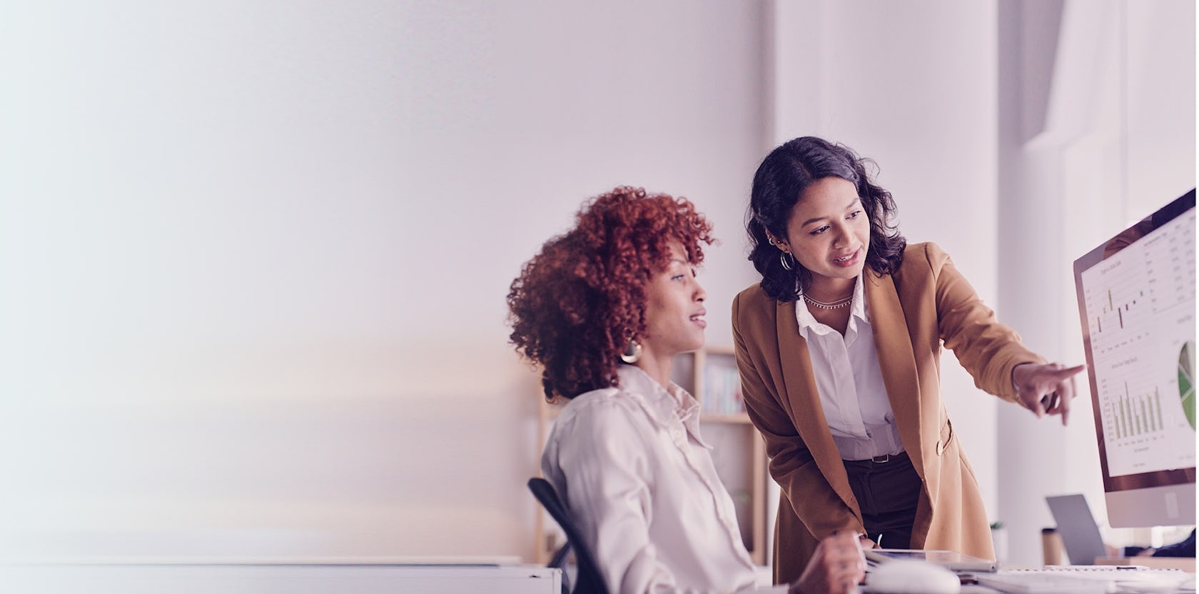 two sales managers looking at a desktop reviewing metrics that show the impact of sales training on their team's performance.