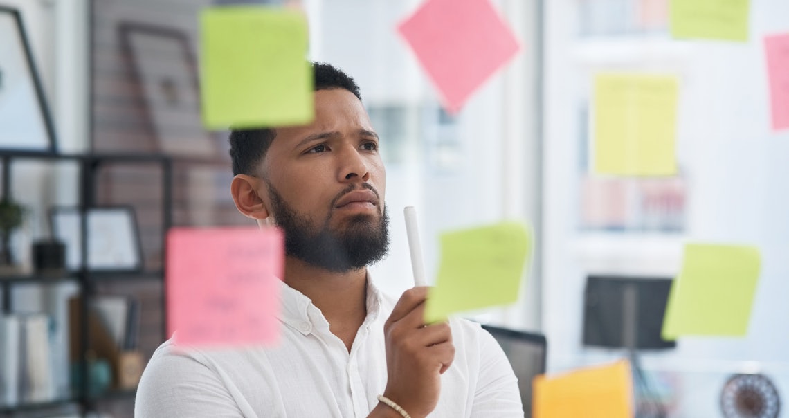young professional black male looking at a bunch of post-it notes that he's using to organize his thoughts as he works to choose a sales management training program