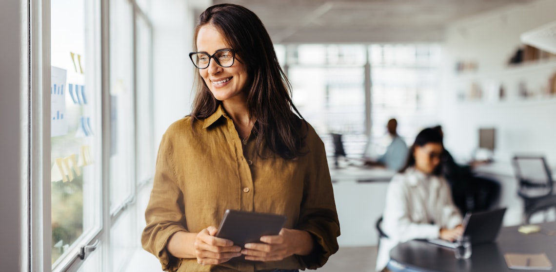 sales woman looking out office window smiling because she has confidence in her selling skills and that confidence is translating into real-world results