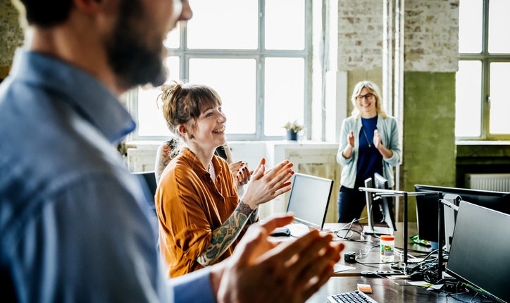 A team of sellers in an open-concept office space celebrating another team win from their desks. The win is a result of a strong sales culture.