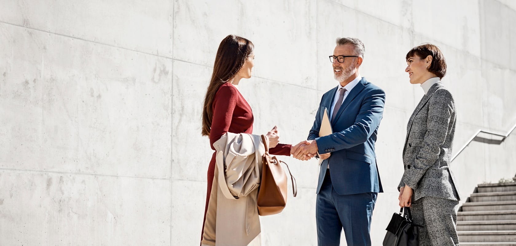 stylish male and female business professionals shaking hands outside a modern office building on a sunny day symbolizing richardson's deep alliance partnerships in the sales improvement industry