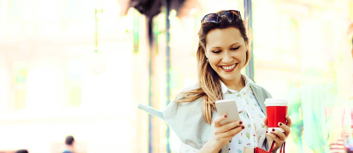 young female sales professional using her cell phone on a city street to complete a simple training reinforcement exercise on Richardson's QuickCheck solution.