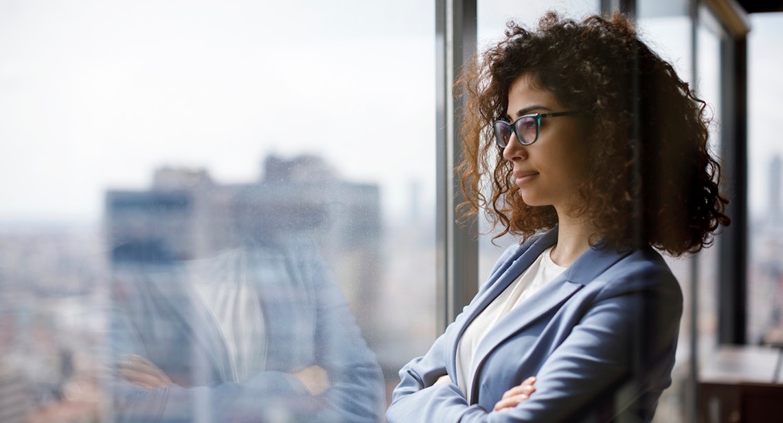 female sales manager pensively looking out of an office window thinking of how she can use her sales management science to empower her sellers to reach their next level of success.