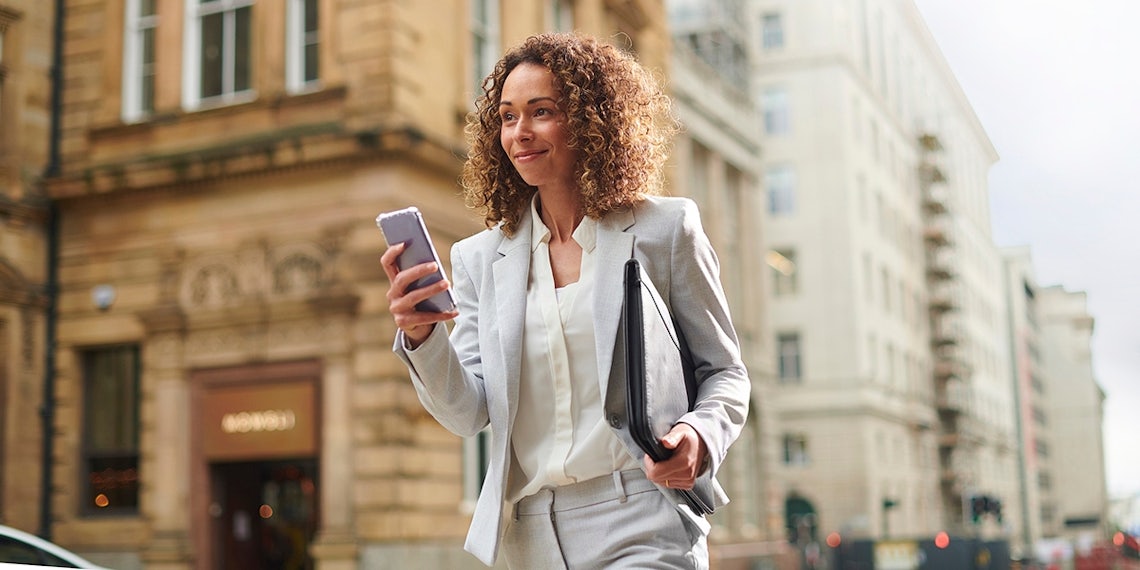 saleswoman walking down the street using her phone to experience a microlearning training module ahead of a meeting.