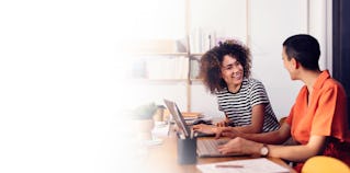 a young female sales professional and her manager sitting at a desk with a computer in an airy office working on their channel partner management plan using the skills they learned in richardson's channel partner management training program