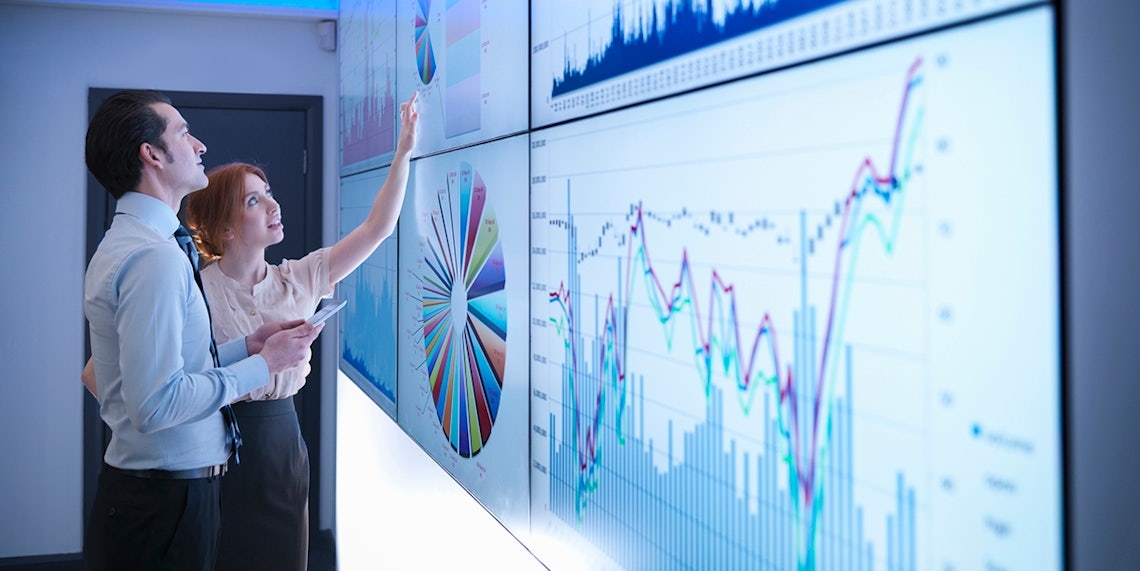 female sales manager and male sales person examining CRM data on a large video wall to diagnose the sales pipeline and find opportunities to improve results