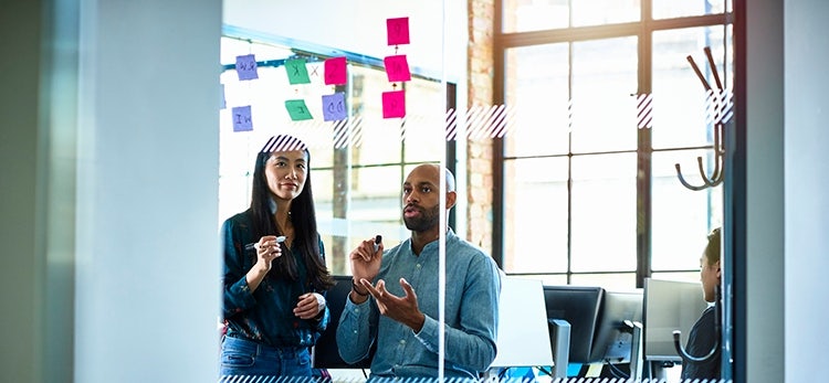 two sales enablement professionals outlining their sales enablement framework on a white board with post-its