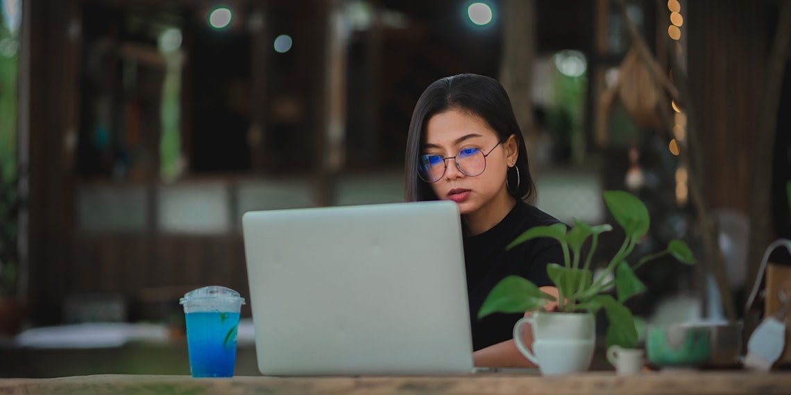 woman sitting at laptop in coffee shop concentrating on using business writing best practices for sales professionals to craft an attention-grabbing email to a client