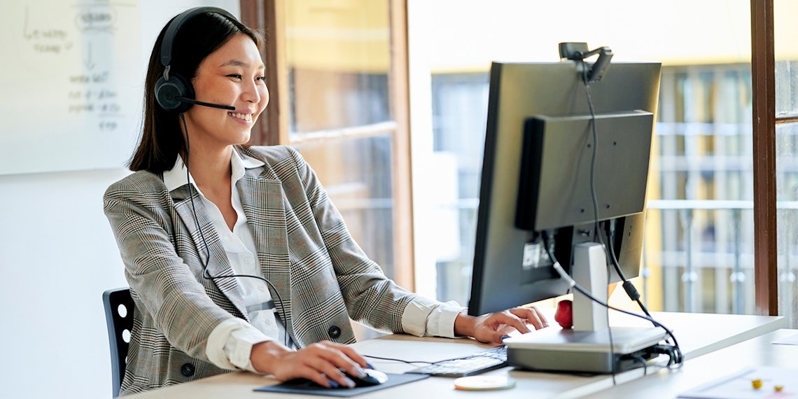 customer service professional sitting at a desk with a telephone headset talking with a customer to better explore their needs so she can offer insights and expanded options to resolve them.